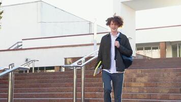 Handsome young man student walking down the stairs near university or office building. Hold books. Slow motion video