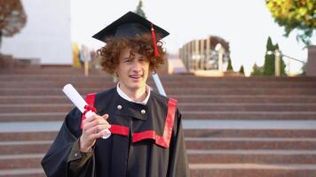 Portrait of happy guy on her graduation day University. Curly graduate with braces smiles near the college. Education and people video