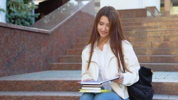 Young girl student sits on the stairs reads books in a university campus video