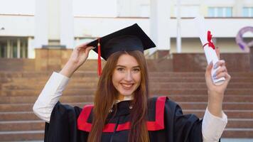 ein Universität weiblich Absolvent steht im ein Meister Mantel mit ein Diplom im seine Hand und hält auf ein Meister Hut video