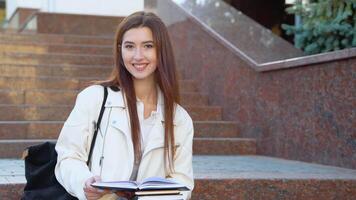 jong meisje leerling zit Aan de trap leest boeken in een Universiteit campus video