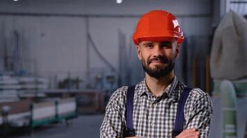 Porträt von bärtig Fabrik Arbeiter im schützend Helm suchen beim Kamera während Stehen im Werkstatt video