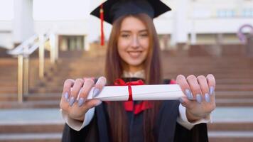 The university female graduate stands in the Master's Mast and holds a diploma in front of the camera. The focus of the camera is on scroll video