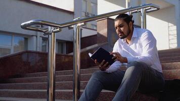 joven indio estudiante se sienta en el pasos y lee libros video