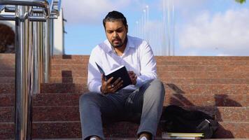 Indian student sits on the stairs reads books in a university campus video