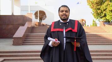 Happy indian student graduate stands on the stairs with diploma and hat in a university campus video