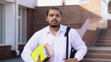 indiano masculino aluna com livros e bolsa, perto Faculdade video