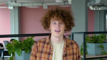 Happy redhead male freelancer with braces smiling at camera and walk in co working space video