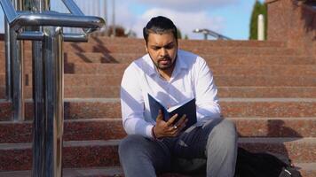 Young Indian student sits on the steps and reads books video