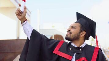 contento graduado. contento indio hombre en graduación vestidos sostiene un diploma video