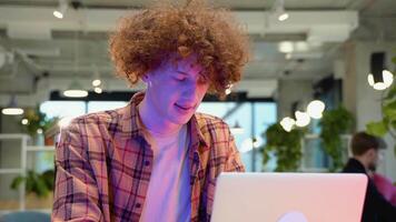 giovane programmatore con bretelle seduta a un' tavolo nel un' bar e Lavorando su un' il computer portatile video