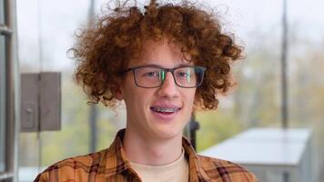 Portrait of happy male freelancer in optical eyewear for vision correction and braces smiling at camera during break from web working online, cheerful hipster blogger sitting video