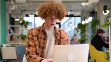 Surprised male freelancer during web working online. Red -haired curly hipster blogger sitting in cafe with laptop computer video