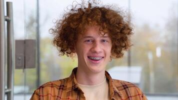 Portrait of happy male freelancer with braces smiling at camera during break from web working online, cheerful hipster blogger sitting in office with laptop computer video