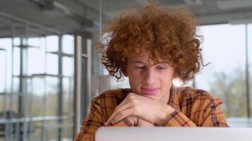 portrait de content Masculin pigiste souriant à caméra pendant Pause de la toile travail en ligne, de bonne humeur branché blogueur séance dans Bureau avec portable ordinateur video