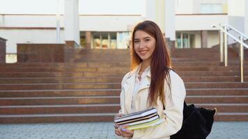 Young girl student smiling near university. Cute girl student holds books. Learning, education concept video
