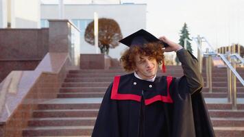 uma jovem engraçado graduado dentro uma mestrado manto tocam brincando com uma chapéu video