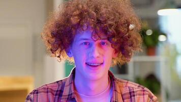 A young red -haired curly man with braces sits in a cafe smiles and looks at the camera video