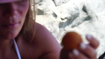 kvinna äter aprikos. närbild porträtt av Lycklig ung kvinna njuter aprikos på solnedgång förbi hav. avkopplande förbi de hav, njuter frukt på strand, ha roligt och Bra humör. resa, turism, semester, video