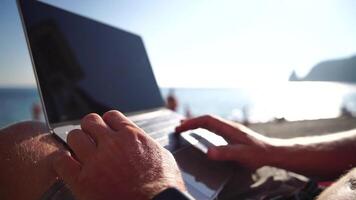 Man laptop sea. Working remotely on seashore. Happy successful man male freelancer working on laptop by the sea at sunset, makes a business transaction online. Freelance, remote work on vacation video