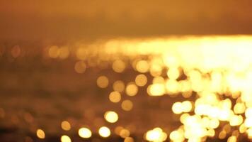 wazig gouden zee Bij zonsondergang. de zon weerspiegelt en sparkles Aan de golven met bokeh, verhelderend de gouden zee. vakantie recreatie concept. abstract nautische zomer oceaan zonsondergang natuur achtergrond. video