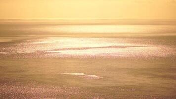abstrakt antenn hav sommar hav solnedgång natur bakgrund. små vågor på lugna vatten yta i rörelse fläck med gyllene bokeh lampor från Sol. Semester, semester och rekreations begrepp. långsam rörelse video