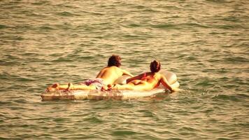 verano vacaciones mujer flotadores en un inflable colchón en calentar puesta de sol tiempo, un agua nadar juguete. positivo contento mujer relajante y disfrutando familia verano viaje Días festivos vacaciones en el mar. lento movimiento video