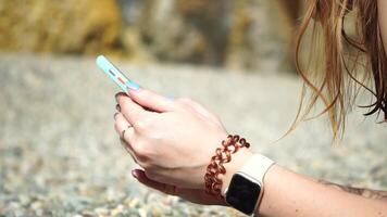 vrouw met smartphone. detailopname van vrouw handen Holding verticaal mobiel telefoon en vegen omhoog vinger toepassing bladzijde tegen achtergrond van zee en strand video