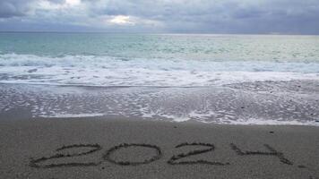 Happy New Year 2025 hand written digit 2024 washed by wave on the sea beach. Abstract background of coming New Year 2025 and leaving year of 2024. video