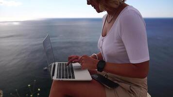 Digital Nomade, Geschäft Frau Arbeiten auf Laptop durch das Meer. ziemlich Dame Tippen auf Computer durch das Meer beim Sonnenuntergang, macht ein Geschäft Transaktion online von ein Distanz. freiberuflich, Fernbedienung Arbeit auf Ferien video