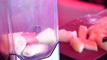 mujer haciendo un Fruta cóctel en un licuadora, batidos preparación con melón y banana. mujer pone cachorros de hielo y piezas de melón dentro un licuadora. sano verano bebida concepto. video