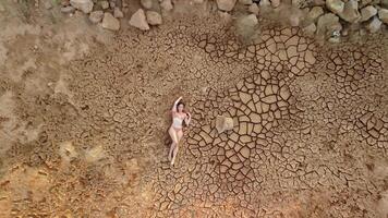 aéreo retrato de hermosa joven dama en bikini acostado en seco agrietado rojo suelo. árido, agrietado rojo suelo sequía y árido clima condiciones. clima y clima cambiar. video