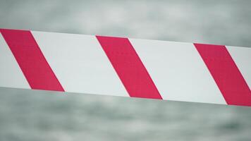 rood wit waarschuwing plakband barrière lint swinging in de wind aan de overkant exotisch zee strand achtergrond zonder mensen. Nee binnenkomst rood wit voorzichtigheid plakband. Nee vakantie concept, vertraagd reis, Nee zomer plannen video