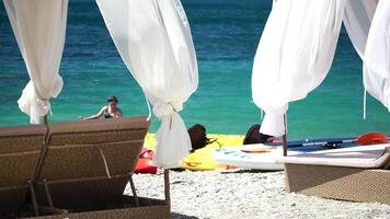 bangalôs mar. de praia salão cama com branco sedoso cortinas. salão cama com marquise às à beira-mar. de praia cadeiras e guarda-sóis. verão período de férias recorrer conceito. video