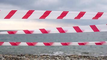 Red white warning tape barrier ribbon swinging in the wind across exotic sea beach background without people. No entry Red White caution tape. No holiday concept, delayed travel, no summer plans video