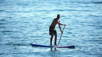 hombre cenar mar. fuerte atlético hombre aprende a paleta cenar en pie en tablero en abierto mar Oceano en soleado día. verano fiesta vacaciones y viaje concepto. aéreo vista. lento movimiento video