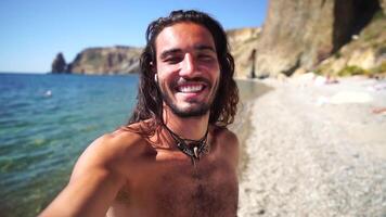 homem verão viagem mar. feliz turista apreciar levando selfie foto ao ar livre para recordações. homem viajante posando em a de praia às mar cercado de vulcânico montanhas, partilha viagem aventura viagem video