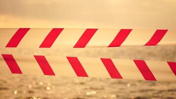 Red white warning tape barrier ribbon swinging in the wind across exotic sea beach background without people. No entry Red White caution tape. No holiday concept, delayed travel, no summer plans video