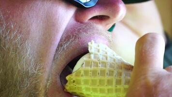 homme en mangeant la glace crème. fermer portrait de Jeune branché homme dans lunettes de soleil en mangeant la glace crème dans été chaud temps sur le plage, avoir amusement et bien ambiance. video