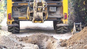 excavador alojamiento un zanja a laico tubería. cerca arriba de un excavador excavación un profundo zanja. un excavador alojamiento un zanja en el campo a laico un agua tubo. video