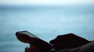 Man sea smartphone. The young man in sunglasses, sunbathing by the sea and spending time on his mobile phone texting with girlfriend, looks at the camera in surprise, sees a news on the phone. video