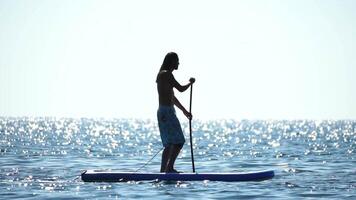 Mens sup zee. sterk atletisch Mens leert naar peddelen sup staand Aan bord in Open zee oceaan Aan zonnig dag. zomer vakantie vakantie en reizen concept. antenne visie. langzaam beweging video