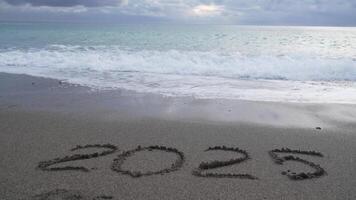 glücklich Neu Jahr 2025 Hand geschrieben Ziffer 2025 gewaschen durch Welle auf das Meer Strand. abstrakt Hintergrund von Kommen Neu Jahr 2025 und Verlassen Jahr von 2024. video