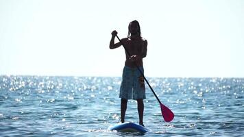 Man Sup Sea. Strong athletic man learns to paddle sup standing on board in open sea ocean on sunny day. Summer holiday vacation and travel concept. Aerial view. Slow motion video