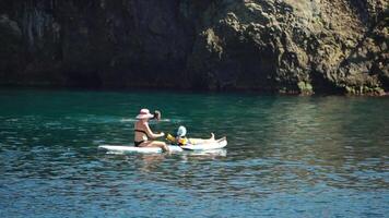 mare donna sup. un' contento positivo donna nel cappello con famiglia rilassante nel mare, aereo indietro Visualizza di famiglia su cenare tavola galleggiante su calma acqua. attivo stile di vita a mare. estate vacanza. lento movimento video