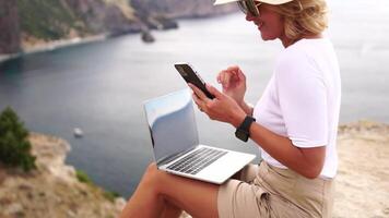 digital nômade, o negócio mulher trabalhando em computador portátil de a mar. bonita senhora digitando em computador de a mar às pôr do sol, faz uma o negócio transação conectados a partir de uma distância. freelance, controlo remoto trabalhos em período de férias video