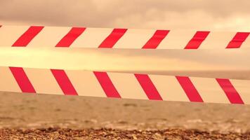 rood wit waarschuwing plakband barrière lint swinging in de wind aan de overkant exotisch zee strand achtergrond zonder mensen. Nee binnenkomst rood wit voorzichtigheid plakband. Nee vakantie concept, vertraagd reis, Nee zomer plannen video