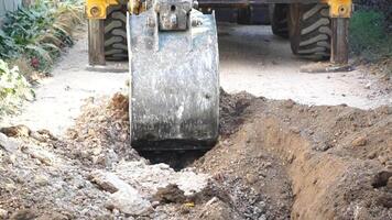 Excavator digs a trench to lay pipes. Close up of an excavator digging a deep trench. An excavator digs a trench in the countryside to lay a water pipe. Slow motion video