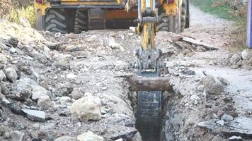 Excavator digs a trench to lay pipes. Close up of an excavator digging a deep trench. An excavator digs a trench in the countryside to lay a water pipe. Slow motion video