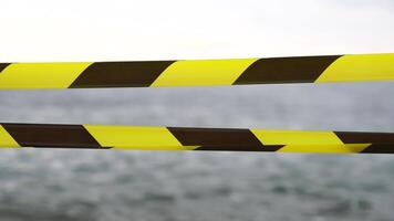 Yellow black warning tape barrier ribbon swinging in the wind across exotic sea beach background without people. No entry Yellow black caution tape. No holiday concept, delayed travel, no summer plans video